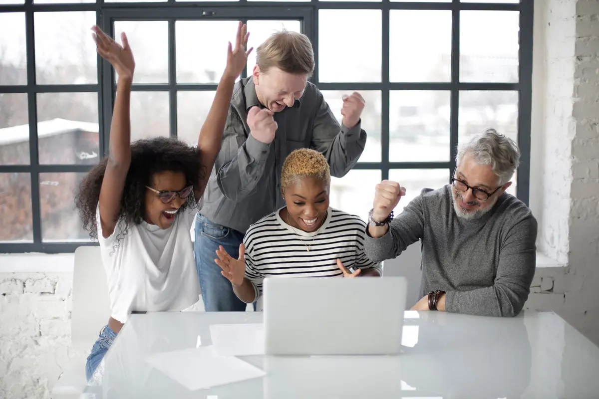 Colleagues of different ages celebrating results at a laptop