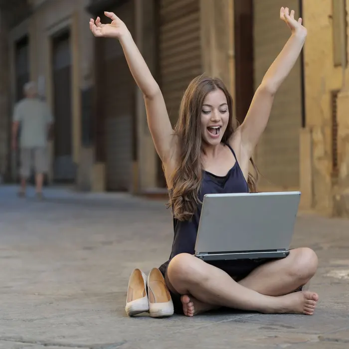 Young founder cheering with her laptop outdoors