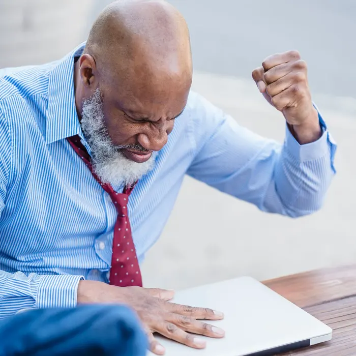 Senior business owner celebrating good news at his laptop